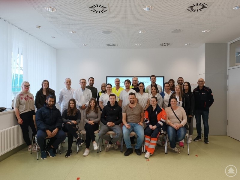 Eine große Gruppe aus Klinikpersonal, Rettungskräften und Übungsteilnehmenden posiert gemeinsam in einem hellen Raum für ein Gruppenfoto.