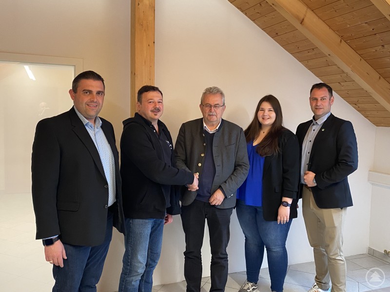 Gratulation zur erfolgreichen ISO/IEC 27001-Zertifizierung: Landrat Josef Laumer (mitte) gratuliert im Beisein von Wiesenfeldens Bürgermeister Andreas Urban (ganz links) und Wirtschaftsförderer Martin Köck (ganz rechts), Siegfried Franke und seiner Tochter. Fünf Personen stehen in einem hellen Raum unter einer Dachschräge nebeneinander und geben sich in der Mitte die Hand. Die Gruppe posiert anlässlich eines Besuchs bei FrankeDATA in Wiesenfelden.